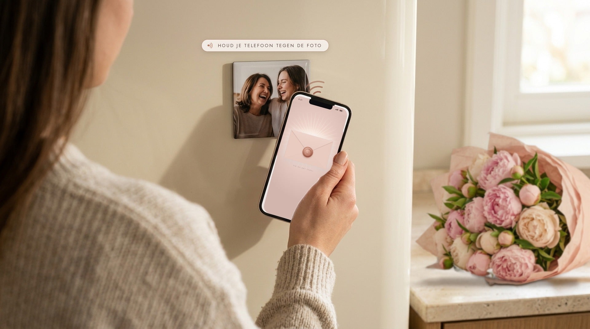 Een vrouw houdt haar telefoon tegen een fotomagneet op de koelkast, met een boeket pioenrozen op het aanrecht